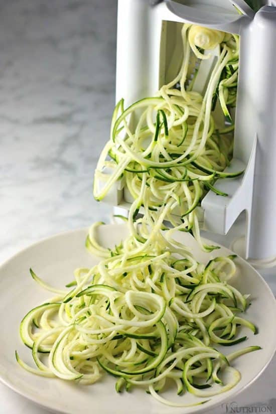 zucchini noodles being spiralized onto a white plate