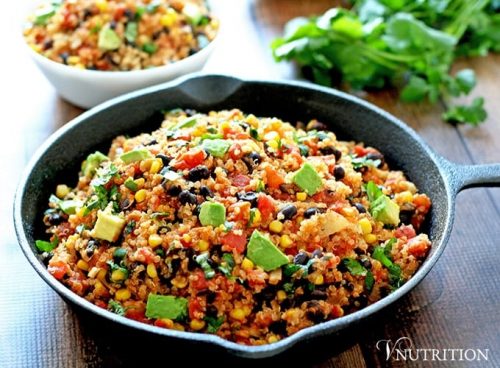 southwest quinoa in skillet with bowl and herbs in background