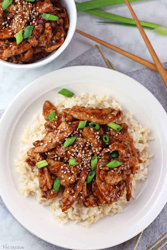 vegan Mongolian beef on a bed of brown rice on a white plate with wooden chopsticks to the side