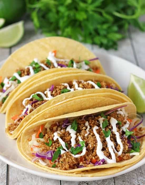 three walnut meat tacos on a white plate with limes and more limes and cilantro in background