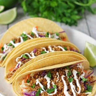 three walnut meat tacos on a white plate with limes and cilantro