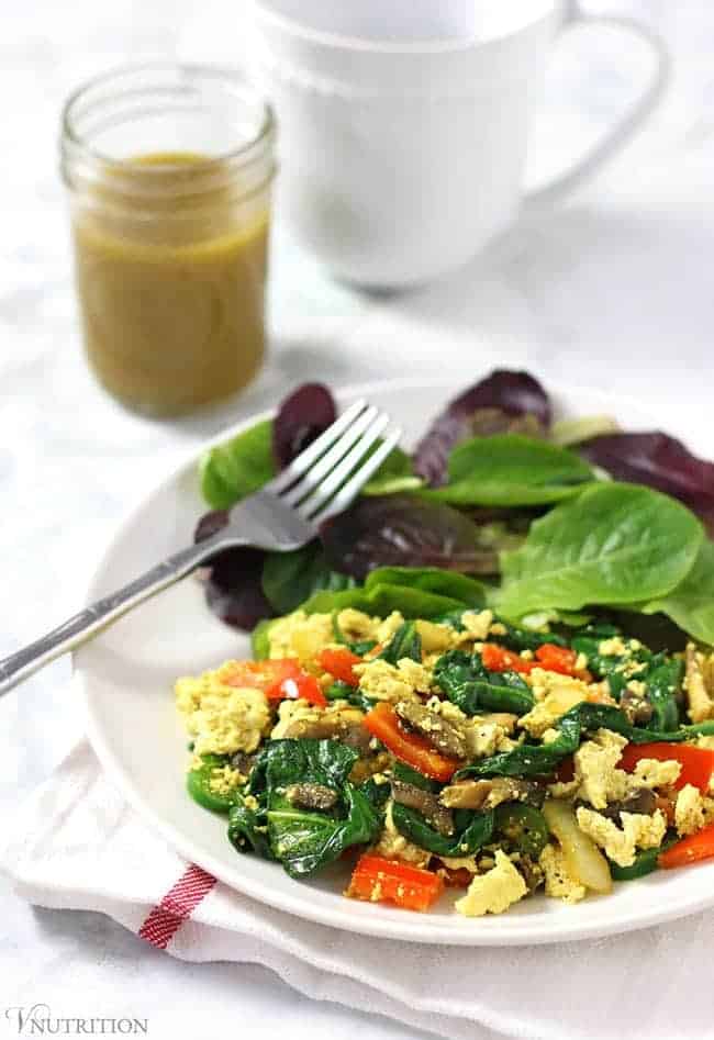 Simple Tofu Scramble with peppers, mushrooms and spinach on a white plate with a side salad and silver fork