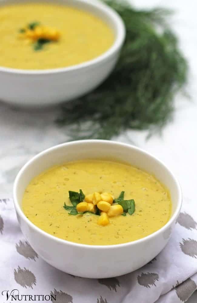 vegan corn chowder in a white bowl topped with corn kernels and fresh herbs.