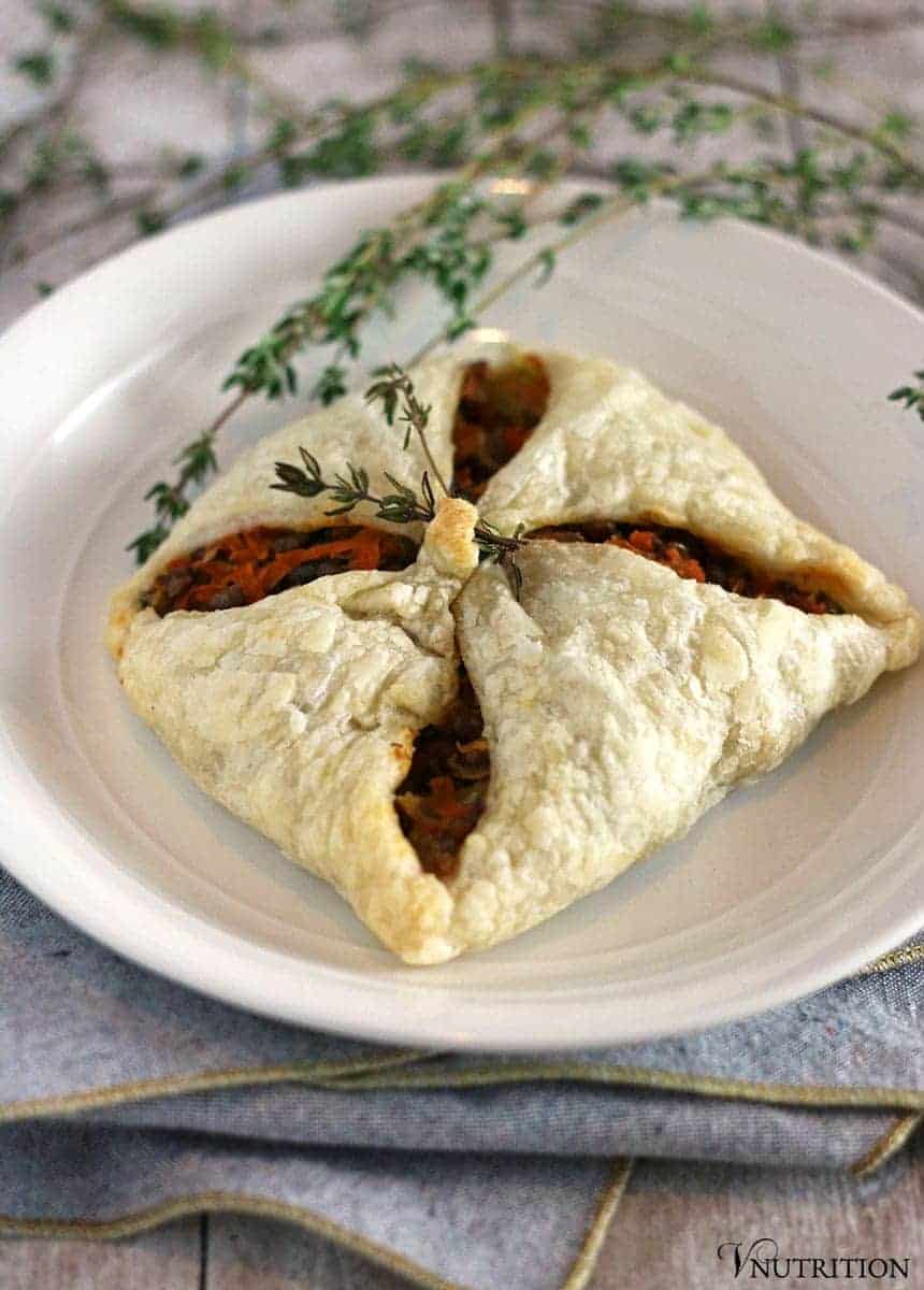 one lentil puff pastry hand pie on a round white dinner plate garnished with fresh sprigs of thyme.