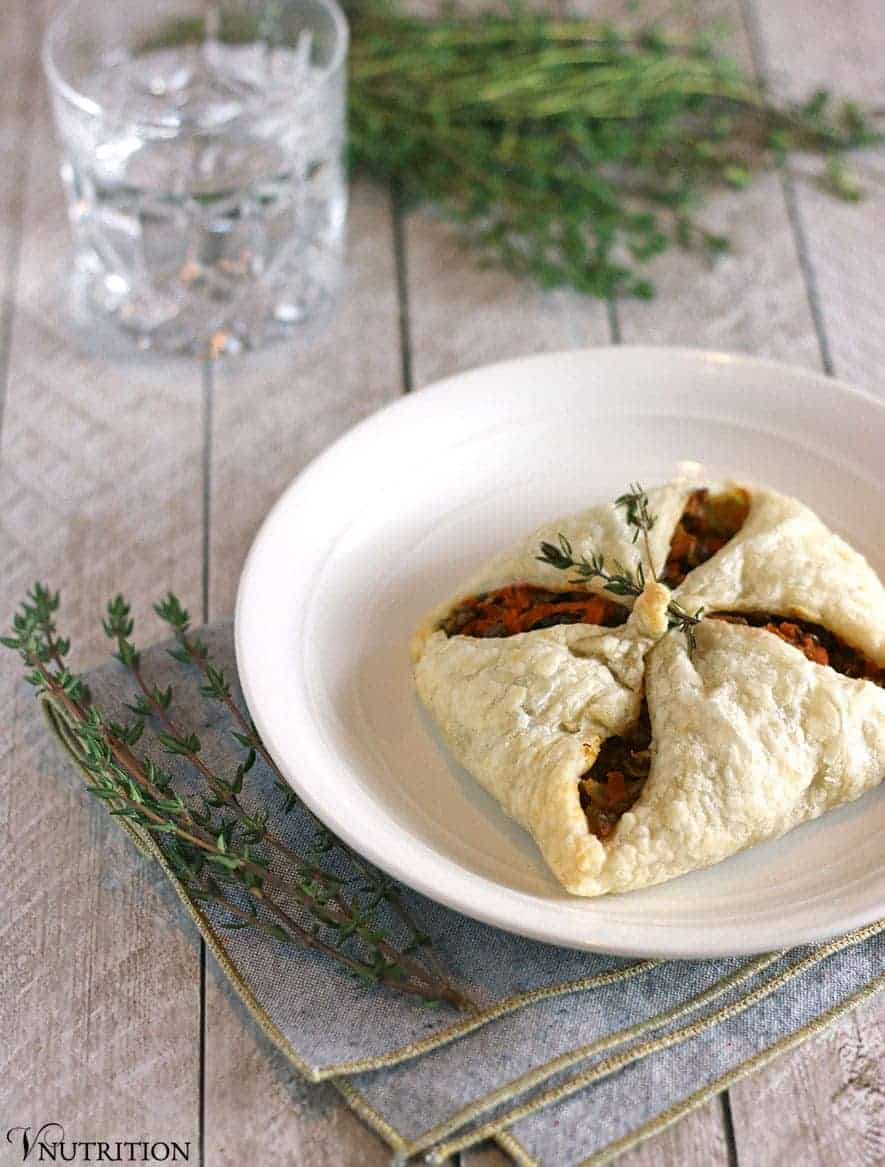 Savory Lentil Puff Pastry Pocket wrapped up like a present on a white dinner plate with a crystal rocks glass and a bunch of thyme as the table centerpiece.