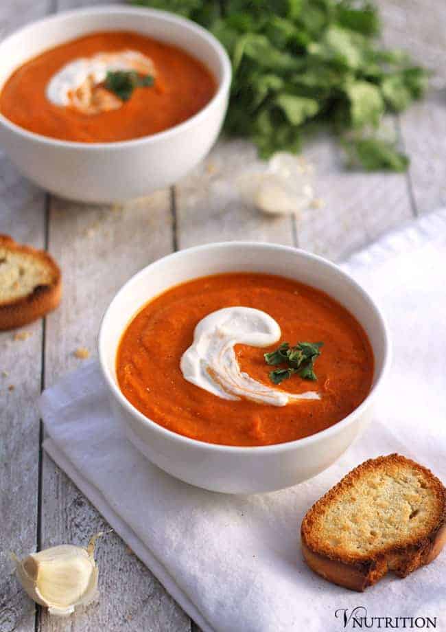 Vegan Roasted Tomato Soup on a table with white napkin, garlic clove and bread