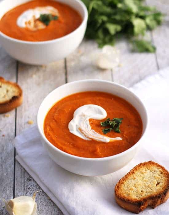 bowl of roasted tomato and chickpea so on white napkin with toasted bread and another bowl of soup with garlic and parsley in background