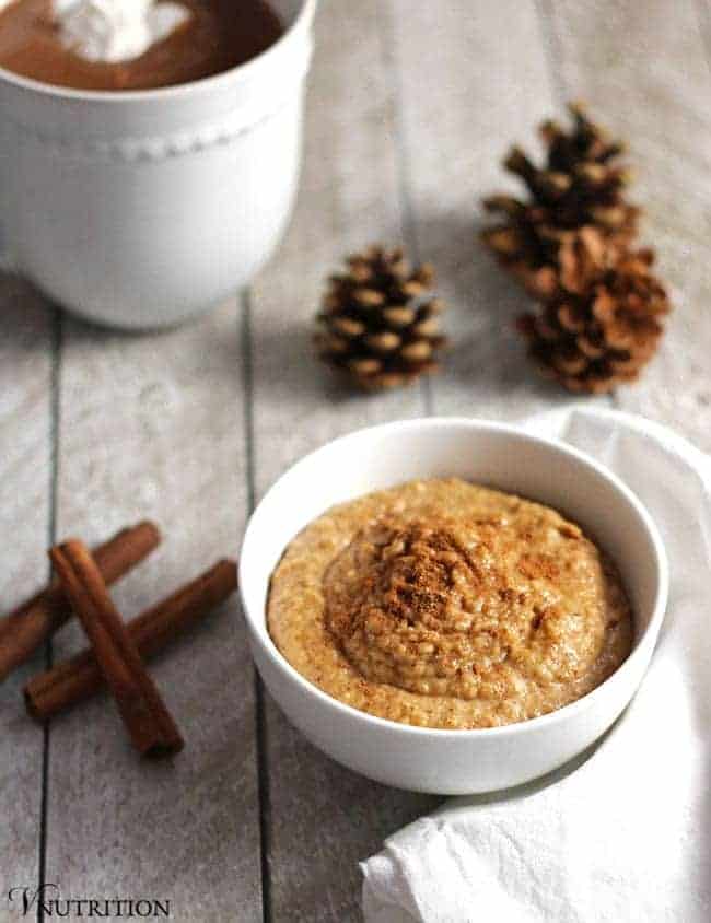 edible snickerdoodle cookie dough in a white bowl next to pine cones and cinnamon sticks.