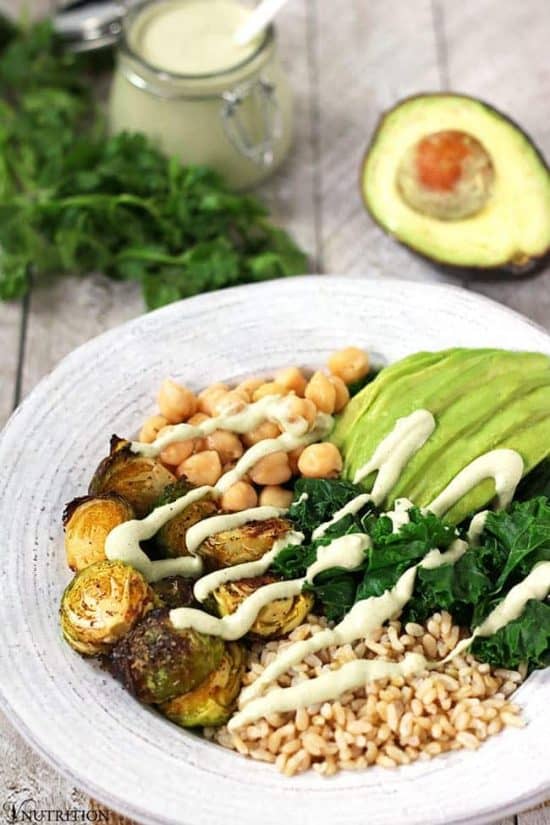 bowl of kale, chickpeas, Brussels sprouts, avocado and rice with creamy green sauce in background