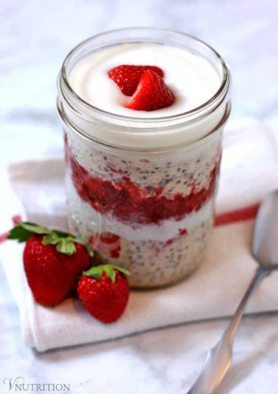 mason jar of strawberries and cream overnight oats topped with strawberries sitting on a napkin with 2 strawberries on side with a spoon