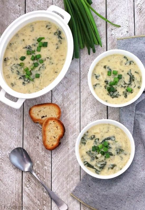 overhead shot of a table with two bowls of vegan potato leek soup, toasted bread and fresh scallions.