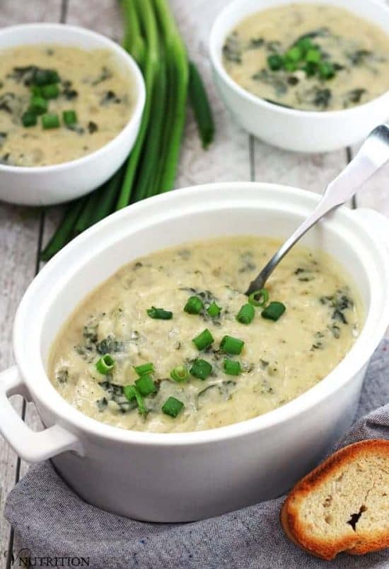 creamy Vegan potato leek Soup in a white bowl with a silver spoon and garnished with green onions.