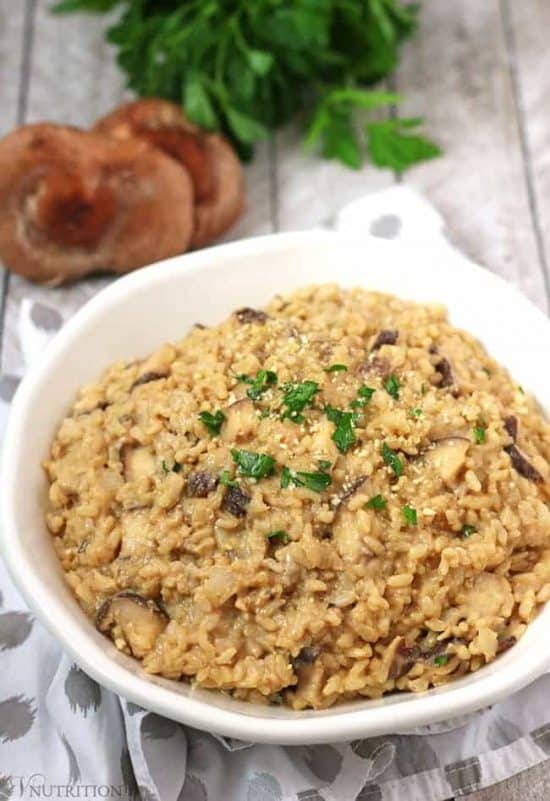 bowl of creamy vegan mushroom risotto in a white bowl with mushrooms and parsley in background