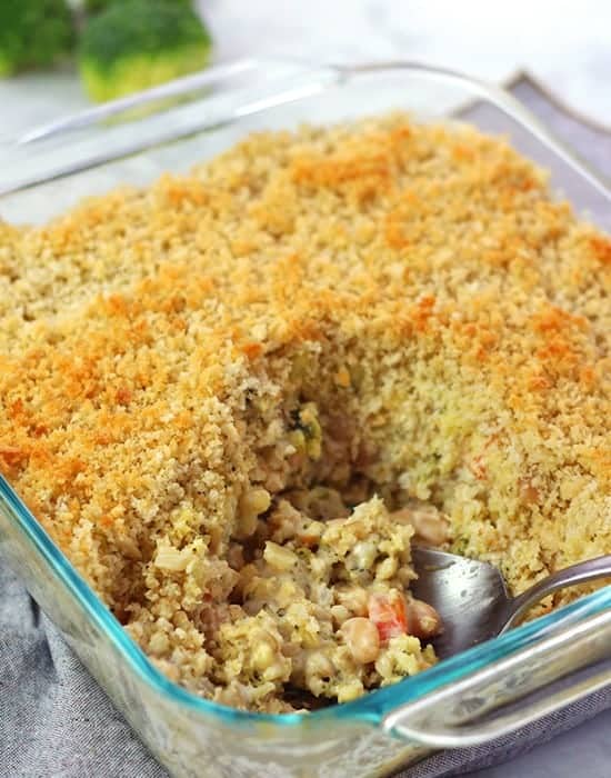 vegetable bean casserole in clear casserole dish with spoon digging in and broccoli in background