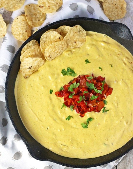 overhead shot of vegan chipotle queso in black skillet topped with salsa on a grey and white napkin with tortilla chips