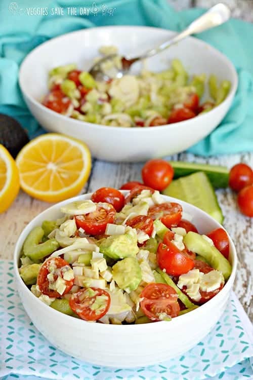hearts of palm salad in foreground with bowl, lemons, tomatoes and cucumber in background for vegan sides for grilling
