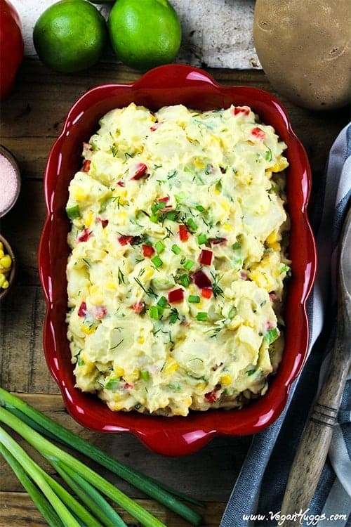 overhead shot of creamy potato salad with utensils on the right and corn, scallions and salt at left for vegan sides for grilling