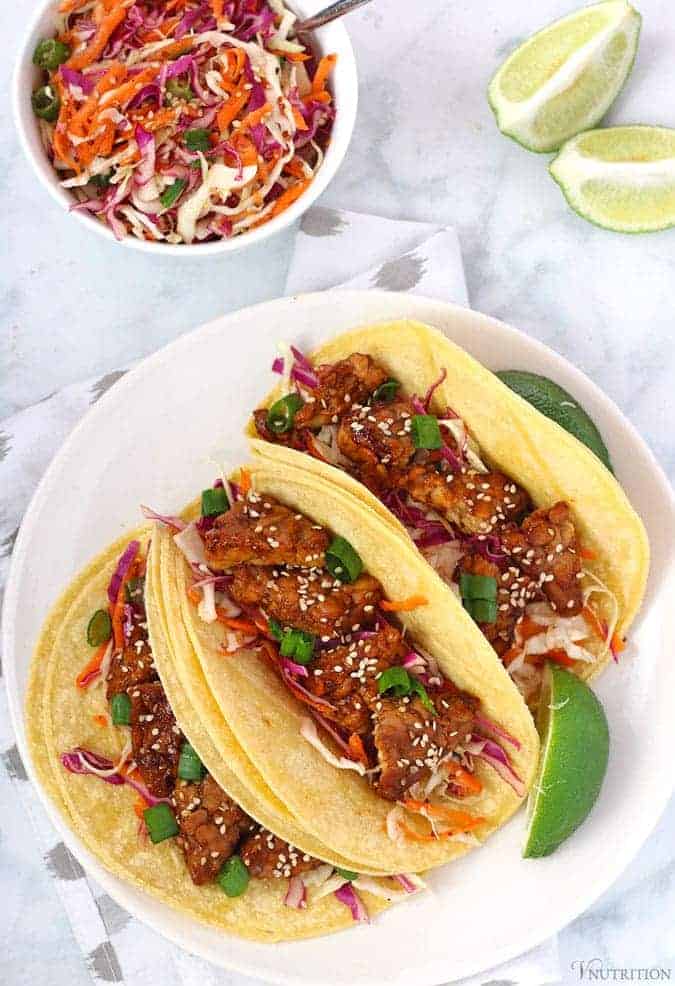 overhead shot of 3 Asian-inspired Tempeh Tacos on a white plate with lime wedges.