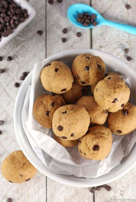 overhead shot of cookie dough protein balls in a white bowl with mini chocolate chips scattered on wooden floor