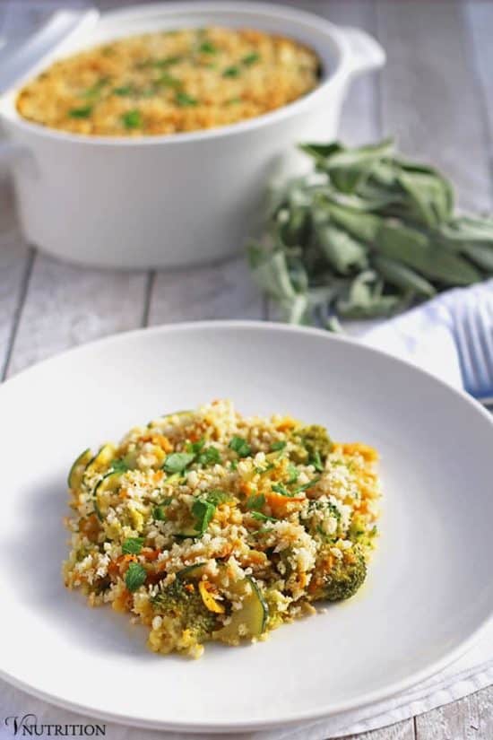 vegetarian Pumpkin Casserole topped with parsley bread crumbs in a white pasta bowl on a whitewashed wood table with a bunch of sage and the casserole dish behind it