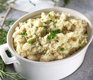 cauliflower mashed potatoes in a white serving crock garnished with parsley.