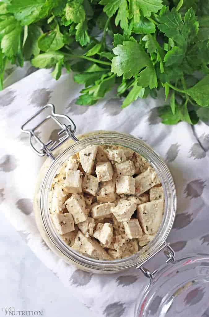 overhead shot of a jar of Tofu Feta on a table with a bunch of parsley to the side.