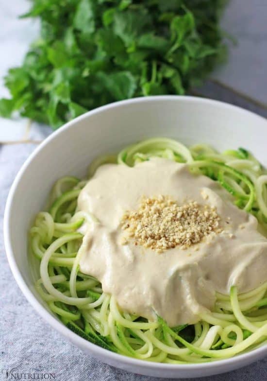 Vegan Zucchini Pasta with Alfredo sauce topped with Parmesan cheese with cilantro in background