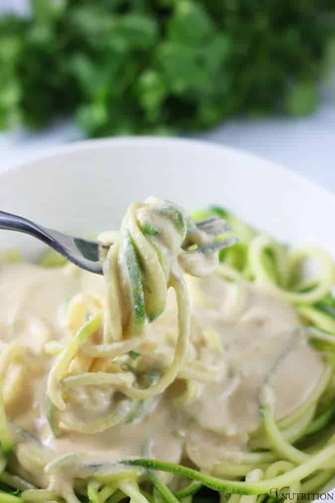 Fork twisting strands of Vegan Zucchini Pasta Alfredo with cilantro in background