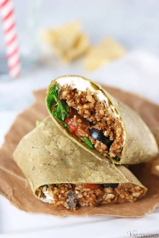 Vegan burrito Wraps on paper bag with chips and water glass with straw in background.