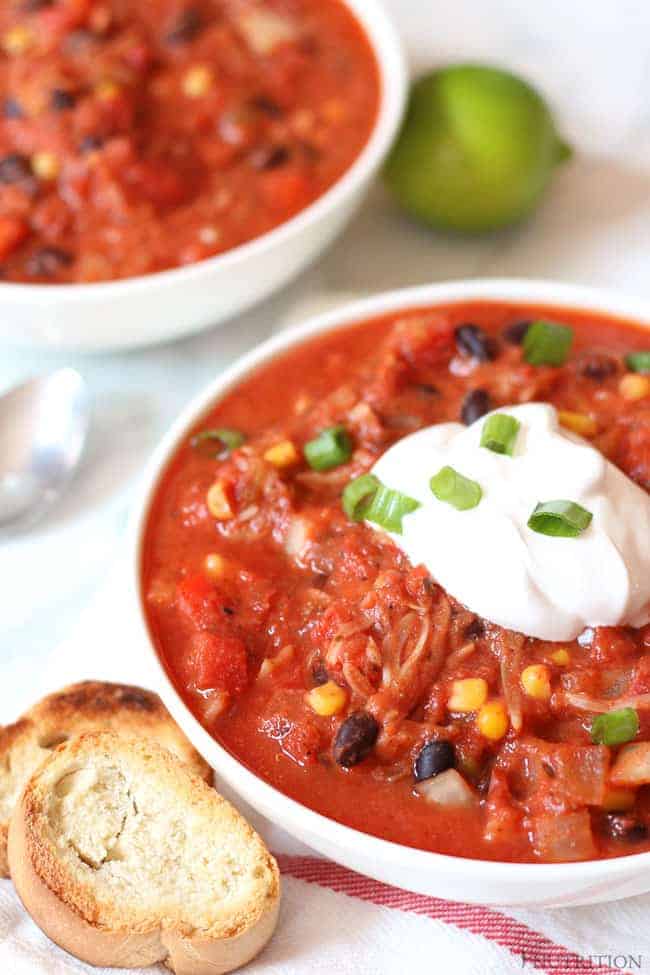 Jackfruit Chili in a white bowl topped with vegan sour cream and sliced green onions.