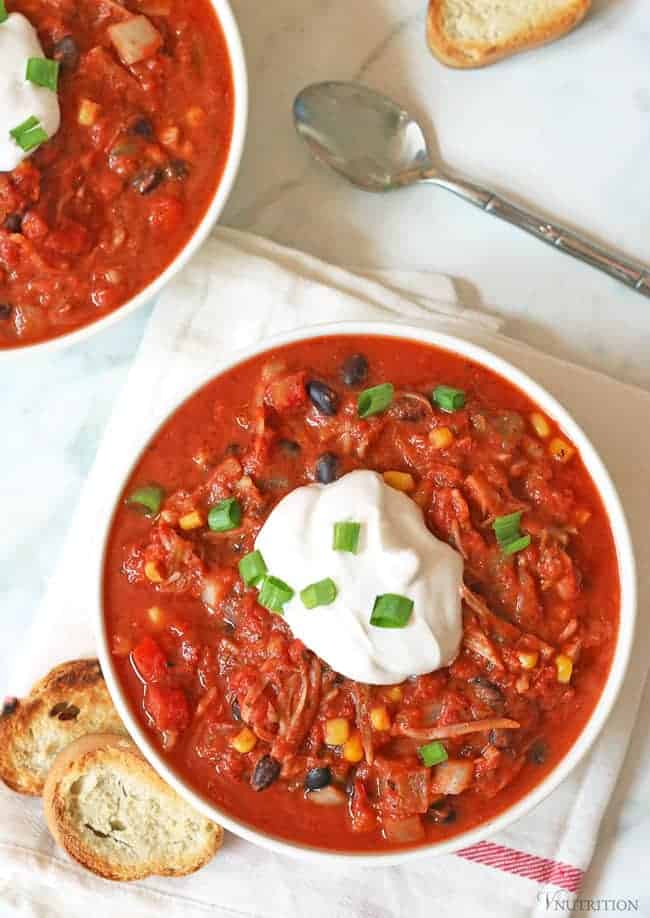 Overhead shot of a bowl of Jackfruit Chili on a table with a kitchen towel and two pieces of toasted baguette.