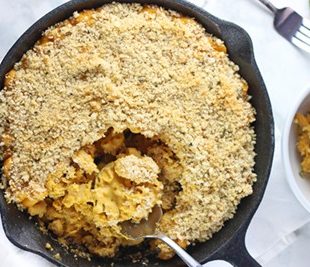 cast iron skillet with a spoon taking a scoop of pumpkin mac and cheese.