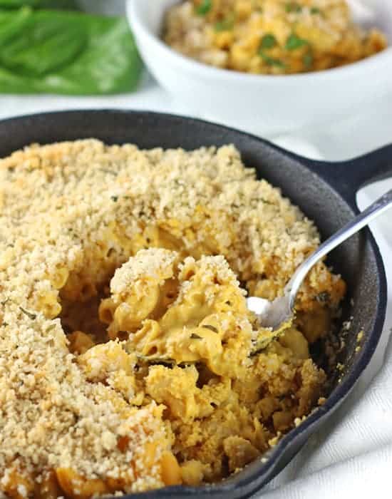 baked vegan pumpkin mac and cheese in a black skillet with fork and a bowl of more pasta in background