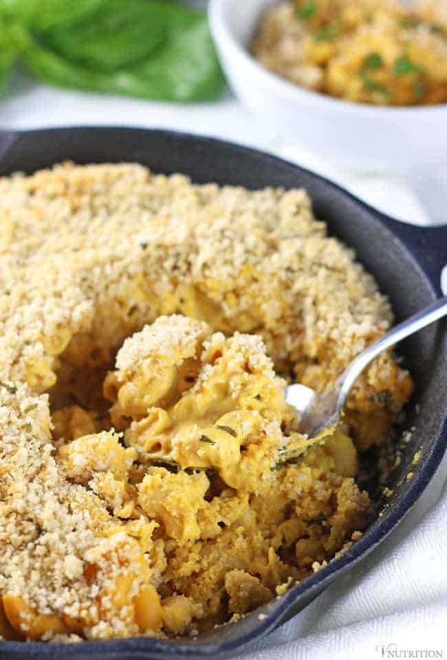 Black cast iron pan with spoon scooping out Vegan Pumpkin Mac and Cheese.