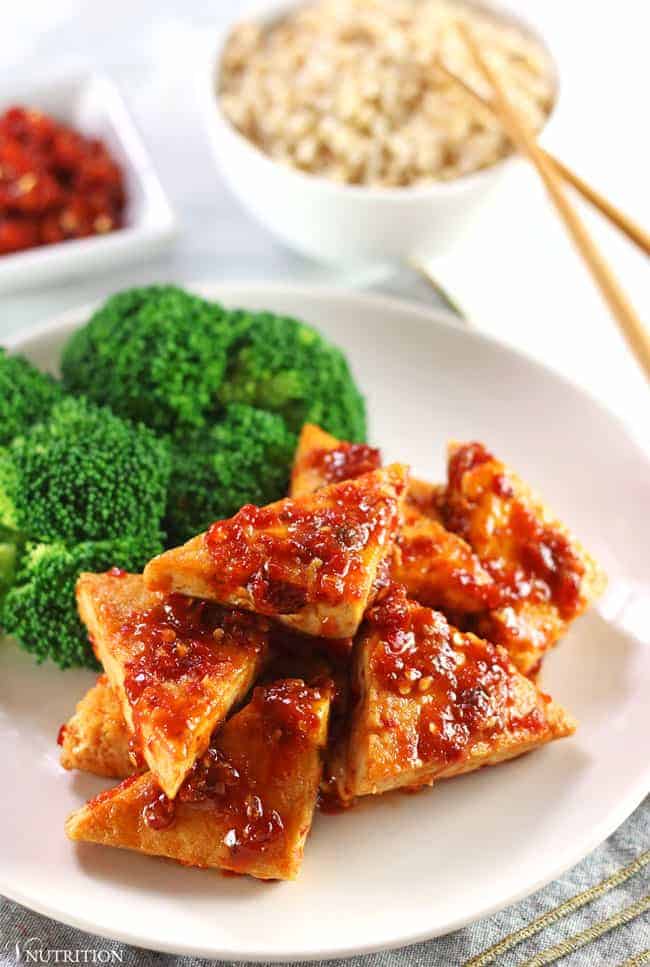 Chili Garlic tofu on a white plate with wood chopsticks and steamed broccoli