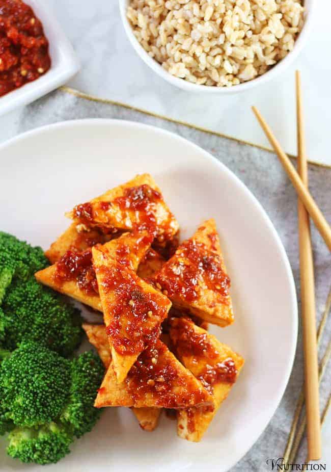 overhead shot of tofu in chili garlic sauce with tofu, chopsticks, brown rice and chili sauce 