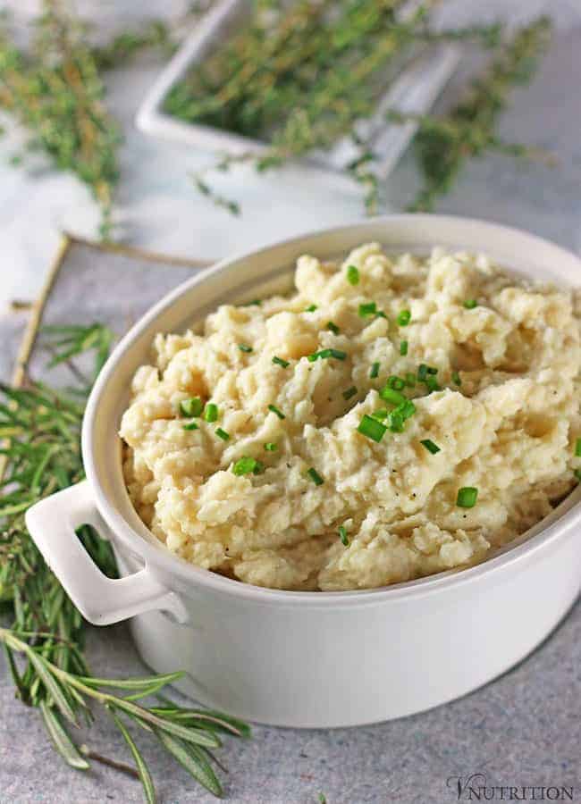 Vegan Cauliflower Mashed Potatoes in white serving bowl on grey napkin with fresh rosemary on the side and thyme in the background