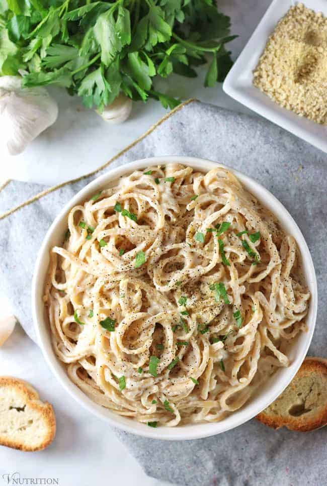 overhead shot of cauliflower alfredo sauce on grey napkin with 2 pieces of bread, parsley, garlic and side of vegan parmesan