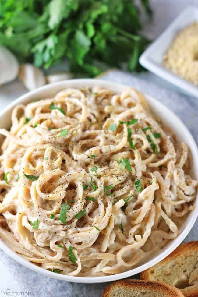 overhead shot of cauliflower alfredo sauce with bread, greens, garlic and vegan parmesan