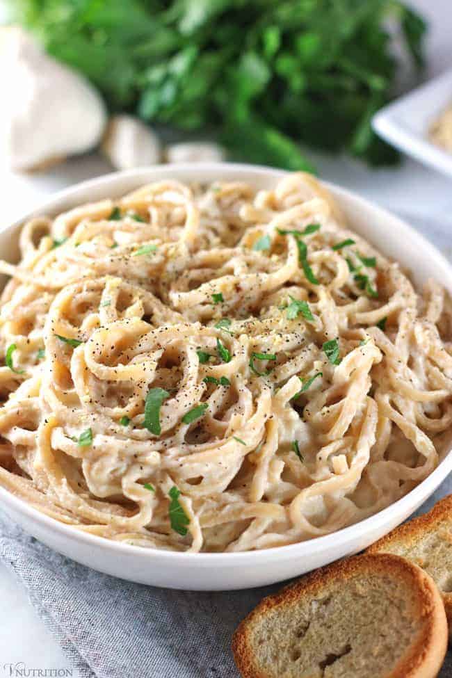 bowl of cauliflower alfredo sauce next to bread with greens and garlic in background