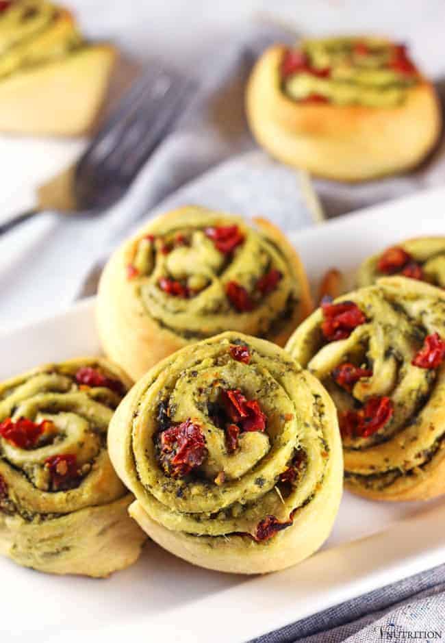 sun dried tomato and pesto Pinwheels appetizers on white plate with grey napkin, fork and two Christmas Pinwheels in background