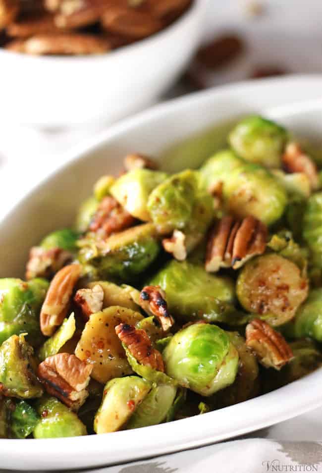 Maple Dijon Brussels Sprouts with toasted pecans in a white serving dish.