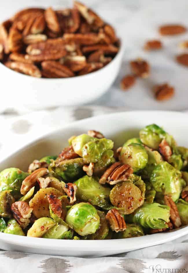 healthy brussels sprouts in white bowl with pecans in background.