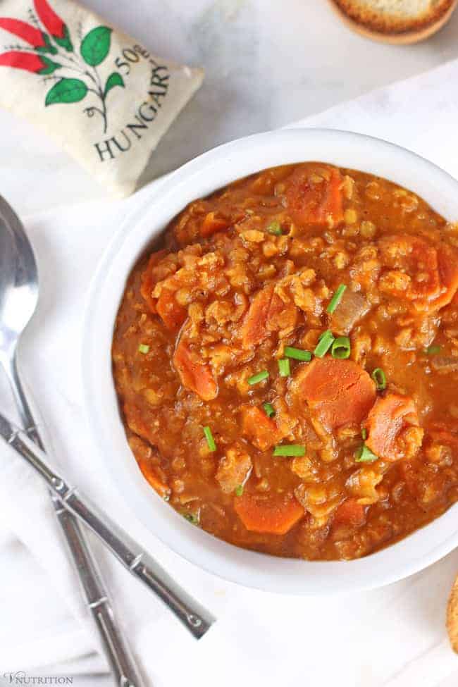 Vegan red lentil soup in a white bowl on a table with a bag of Hungarian paprika.