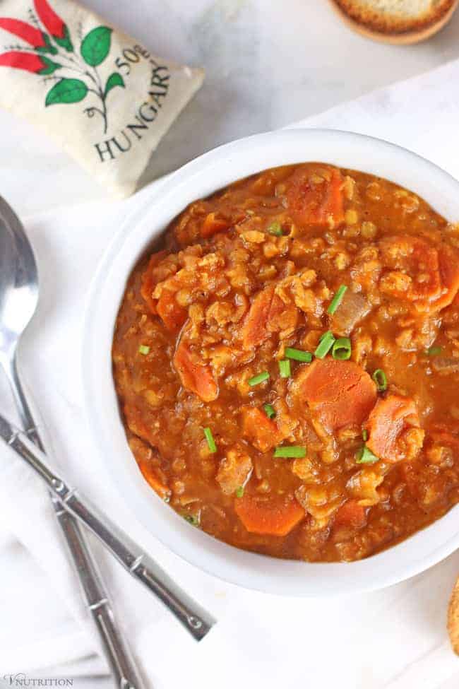 Vegan red lentil soup in a white bowl on a table with a bag of Hungarian paprika. 