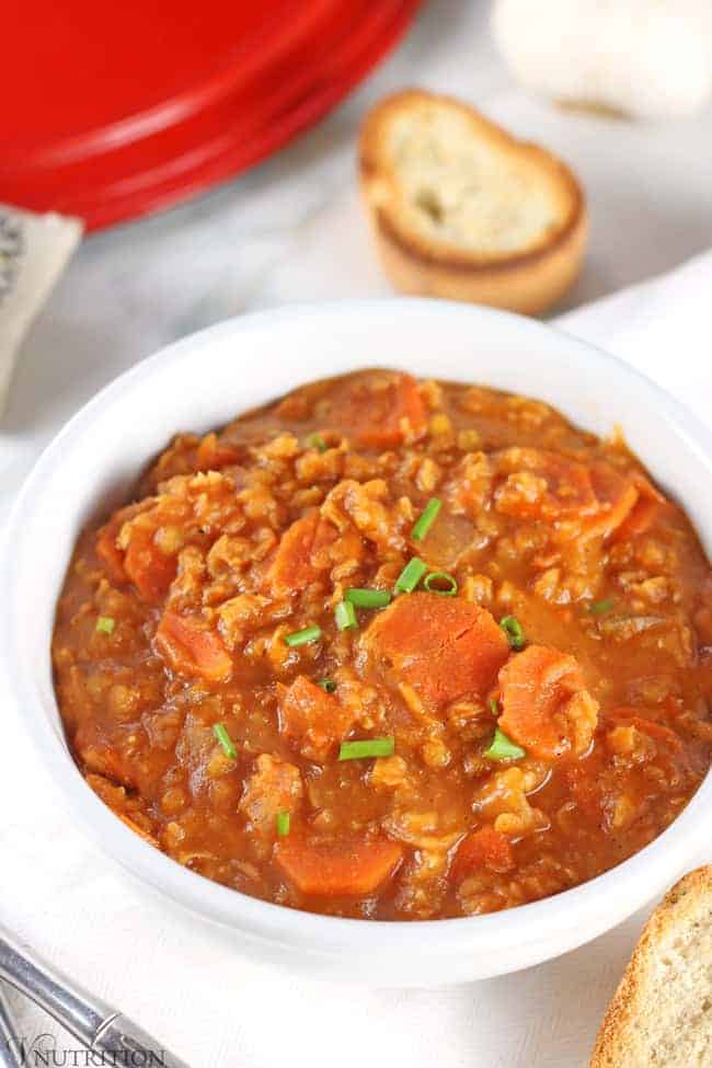 Close up shot of hungarian vegan lentil soup in a white bowl topped with fresh scallions.