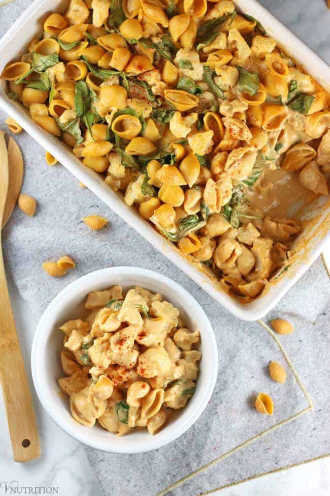 overhead shot of Buffalo Cauliflower Mac and Cheese casserole with a white bowl filled with a serving of it to the side.