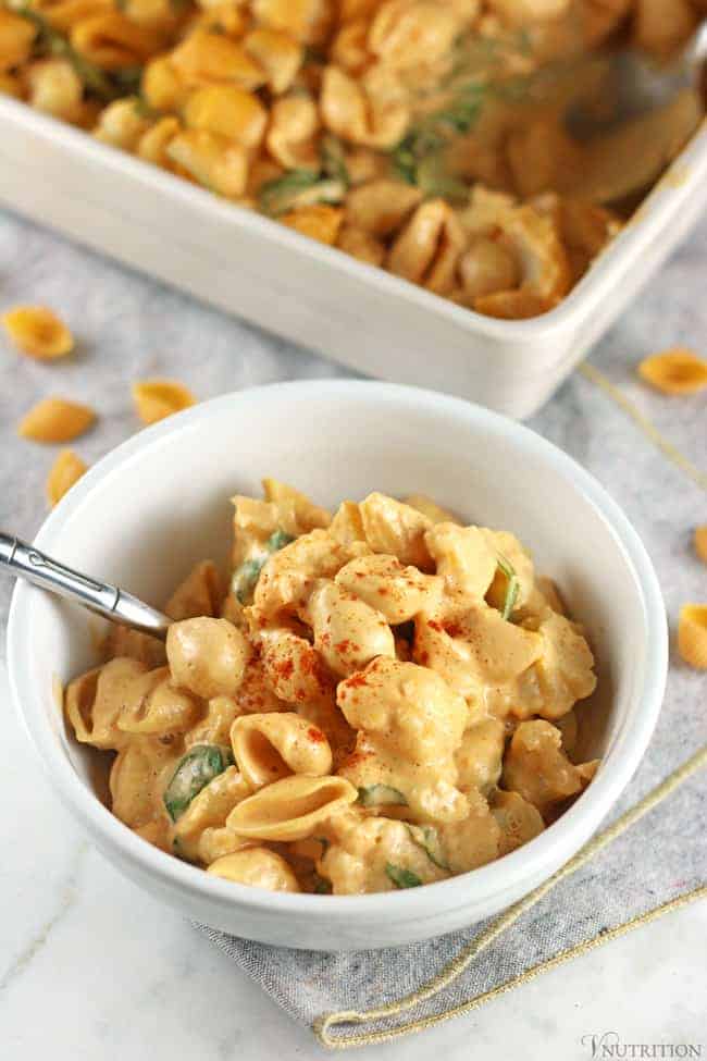 close up shot of a white bowl of Buffalo Cauliflower Mac and Cheese garnished with a sprinkle of paprika and served with a silver spoon.