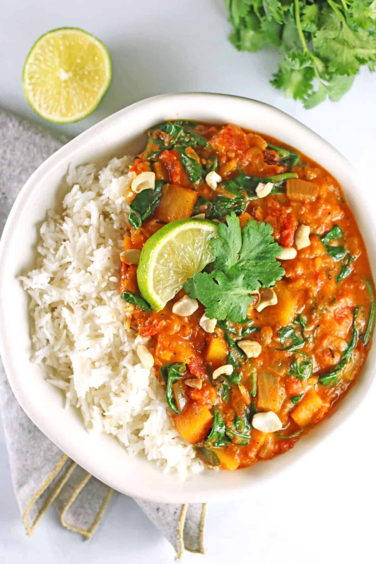 overhead of butternut squash curry with chopped cashews, fresh cilantro and a wedge of lime for serving.