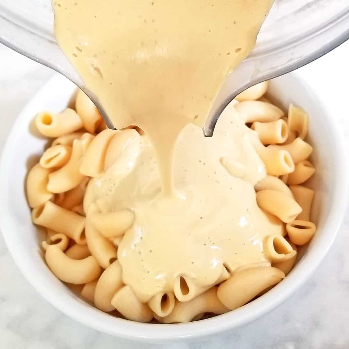vegan cashew cheese sauce being poured over cooked macaroni noodles.
